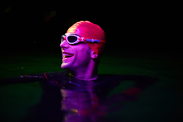 Image showing Authentic triathlete swimmer having a break during hard training on night neon gel light