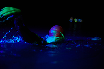 Image showing Authentic triathlete swimmer having a break during hard training on night neon gel light