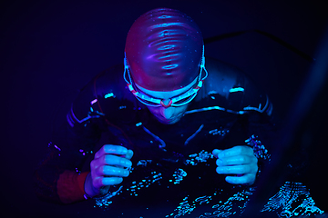 Image showing authentic triathlete swimmer having a break during hard training on night neon gel light