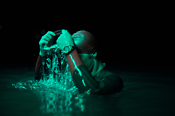 Image showing Authentic triathlete swimmer having a break during hard training on night neon gel light