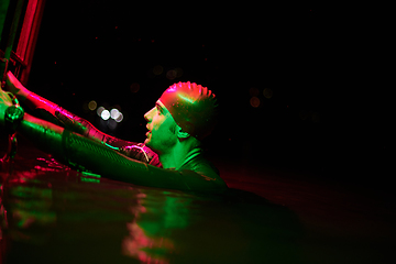 Image showing authentic triathlete swimmer having a break during hard training on night neon gel light