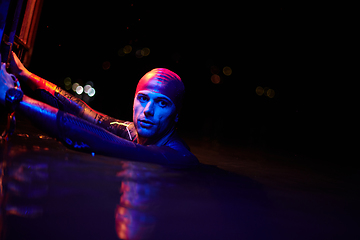 Image showing authentic triathlete swimmer having a break during hard training on night neon gel light