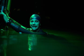 Image showing authentic triathlete swimmer having a break during hard training on night neon gel light