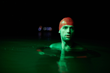 Image showing Authentic triathlete swimmer having a break during hard training on night neon gel light