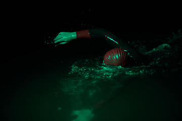 Image showing Authentic triathlete swimmer having a break during hard training on night neon gel light