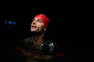 Image showing A determined professional triathlete undergoes rigorous night time training in cold waters, showcasing dedication and resilience in preparation for an upcoming triathlon swim competition