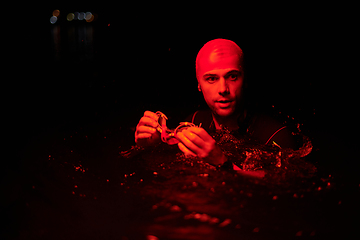 Image showing Authentic triathlete swimmer having a break during hard training on night neon gel light