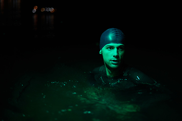 Image showing Authentic triathlete swimmer having a break during hard training on night neon gel light