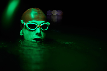 Image showing Authentic triathlete swimmer having a break during hard training on night neon gel light