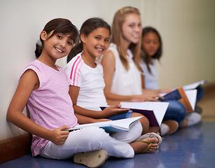 Image showing Girl, students and portrait of friends with books sitting at school in hallway for education or learning. Group of young kids or children smile with textbooks on corridor floor outside classroom