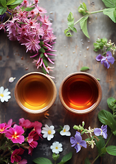 Image showing Two cups with clear amber-colored tea and herbs Ivan-chai, willow-herb, strawberry on wooden table, top view. Vertical. Generative ai.