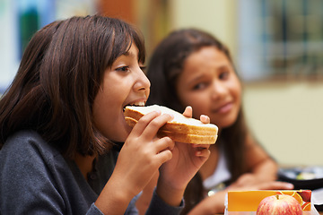 Image showing Hungry girl, student and eating sandwich in classroom at school for meal, break or snack time. Young kid, person or elementary child biting bread for lunch, fiber or nutrition in class during recess