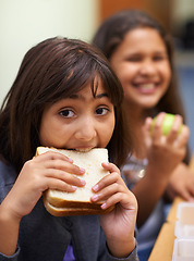 Image showing Hungry girl, portrait and student eating sandwich in classroom at school for meal, break or snack time. Young kid or elementary child biting bread for lunch time, fiber or nutrition in class recess