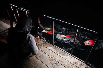 Image showing Videographer taking action shot of triathlon swimming athlete at night