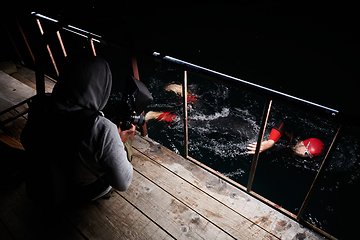 Image showing Videographer taking action shot of triathlon swimming athlete at night