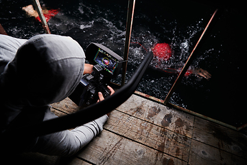 Image showing Videographer taking action shot of triathlon swimming athlete at night