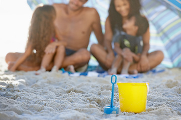 Image showing Family, sand and relax on beach with bucket, spade and umbrella for playing by ocean coast. Blue and yellow toy on sandy shore with people in fun bonding, shade or outdoor holiday weekend together