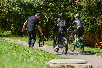 Image showing A professional videographer skillfully captures the joyous journey of a couple on bicycles through the park, blending cinematic expertise with the natural allure of outdoor adventure