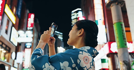 Image showing Woman, phone photography and buildings in night, city or street for architecture, vacation and web blog. Japanese, person and happy for holiday, smartphone or journey with social media in Tokyo