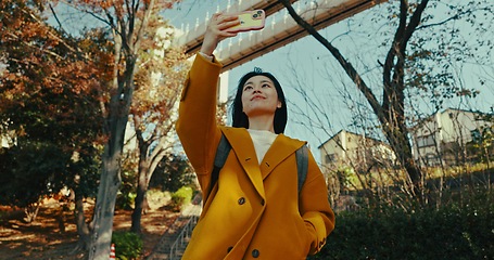 Image showing Japanese woman, selfie and smartphone in city with happiness, holiday adventure and wellness by technology. Person, smile or fashion in tokyo park by outdoor, autumn leaves or urban town with mobile