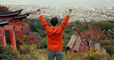 Image showing Man, fist celebration and mountain with view, city and torii gates at Fushimi Inari shrine for shinto religion. Person, hiking and cheers by trees, pillar or achievement on spiritual journey in Kyoto