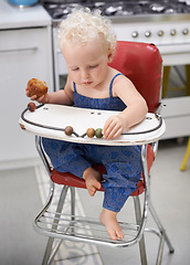 Image showing Child, high chair and eating cupcake, food and breakfast sweets at home in kitchen. Young kid, hungry toddler and muffin dessert, sugar and pastry snack for cute adorable girl in house in the morning