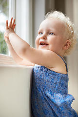 Image showing Happy, window and baby with smile standing against glass or wall in family home learning to walk. Girl, female toddler and young cute kid at house with childhood development or natural growth alone