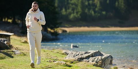 Image showing Athletic man maintains his healthy lifestyle by running through the scenic mountain and lakeside environment, showcasing a commitment to fitness and well-being