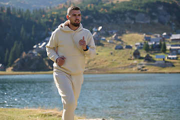 Image showing Athletic man maintains his healthy lifestyle by running through the scenic mountain and lakeside environment, showcasing a commitment to fitness and well-being