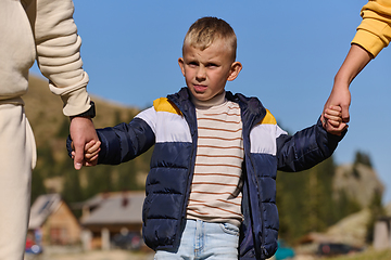 Image showing A close-up shot features a young boy walking hand in hand with his parents , as they joyfully explore the wonders of nature together, creating lasting memories of familial love and outdoor adventure