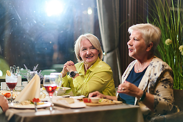 Image showing Elderly friends share a delightful dinner, filled with laughter, joy, and the warmth of enduring friendship, epitomizing the timeless pleasure of companionship in a contemporary setting