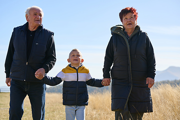 Image showing Elderly couple enjoys a leisurely stroll in nature with their grandchild, creating precious moments of intergenerational bonding amidst the serene and picturesque surroundings