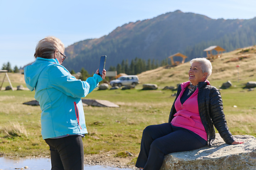 Image showing An elderly pair of women captures a timeless moment on their smartphones, blending technology with the serene beauty that surrounds them