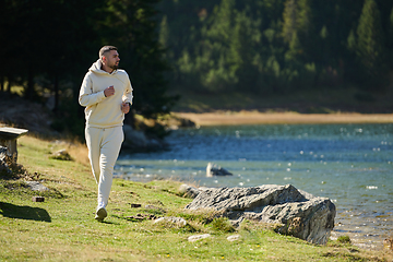 Image showing Athletic man maintains his healthy lifestyle by running through the scenic mountain and lakeside environment, showcasing a commitment to fitness and well-being