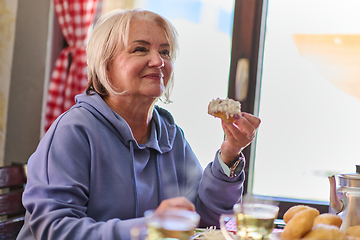 Image showing Elderly woman finds pure joy in the early morning as she savors a wholesome breakfast on the porch of her rustic cottage, embracing the serenity of nature that surrounds her