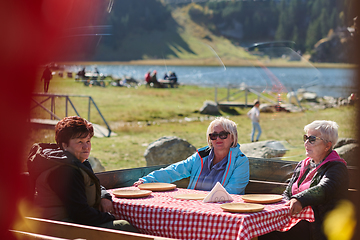 Image showing A group of senior friends engages in lively conversation with the waitress, discussing their meal preferences and savoring the delightful camaraderie that accompanies their dining experience