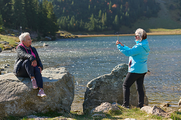 Image showing An elderly pair of women captures a timeless moment on their smartphones, blending technology with the serene beauty that surrounds them