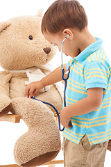 Image showing Boy child, teddy bear and stethoscope in studio for playing doctor, listening and wellness by white background. Kid, healthcare game and development with plushie toys, medical check or consultation