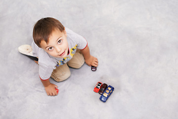 Image showing Car, toys and portrait of kid playing for learning, development and fun at modern home. Cute, top view and sweet young boy child enjoying game with vehicles on floor for childhood hobby at house.