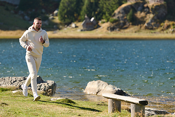 Image showing Athletic man maintains his healthy lifestyle by running through the scenic mountain and lakeside environment, showcasing a commitment to fitness and well-being