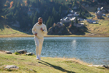 Image showing Athletic man maintains his healthy lifestyle by running through the scenic mountain and lakeside environment, showcasing a commitment to fitness and well-being