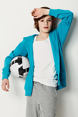 Image showing Soccer, casual and portrait of teenager in a studio for sports training or exercise with style. Serious, fashion and boy kid athlete with football confidence and trendy outfit by white background.