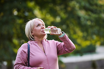 Image showing An elderly woman drinks water after a hard workout in nature