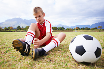 Image showing Boy, soccer player and ball with shoe laces, field and ready for game, shoes and child. Outdoor, playful and sport for childhood, person and athlete for match, alone and outside on football pitch