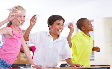 Image showing Happy kids, students and paper plane in classroom on break at desk for fun games to throw or relax. Diversity, distraction or children playing with smile, origami jet or airplane in school together