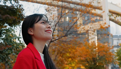 Image showing Japanese woman, thinking and outdoor in city for travel in autumn with trees and happiness. Park, forest and person in Tokyo nature on commute in morning with freedom, wellness and adventure in woods