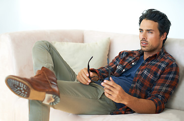 Image showing Man, thinking and glasses on sofa in home with ideas in morning or living room for eyesight and healthcare. Hipster, person or sitting on couch with vision, eyewear or spectacles to see clear