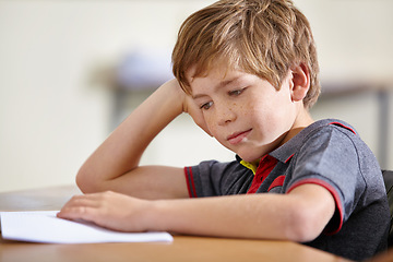 Image showing Class, notebook and bored child at desk, learning and education with school exam. Reading book, studying for test and boy student in classroom with knowledge and thinking with depression on project.