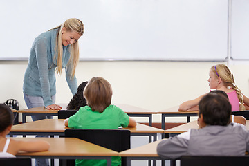 Image showing Teacher, children and classroom for education, learning and writing or language development with support at desk. Happy woman with kids for teaching, helping with knowledge and questions at school