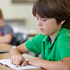 Image showing Classroom, notebook and child at desk, reading and education for learning at school exam. Book, studying for test and boy student in classroom with knowledge and thinking with depression on project.